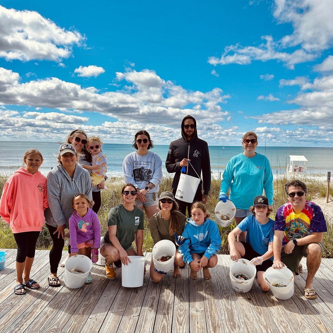 13 volunteers of various ages pose on a boardwalk at the Western Beach Access in Emerald Isle, North Carolina after a beach cleanup.